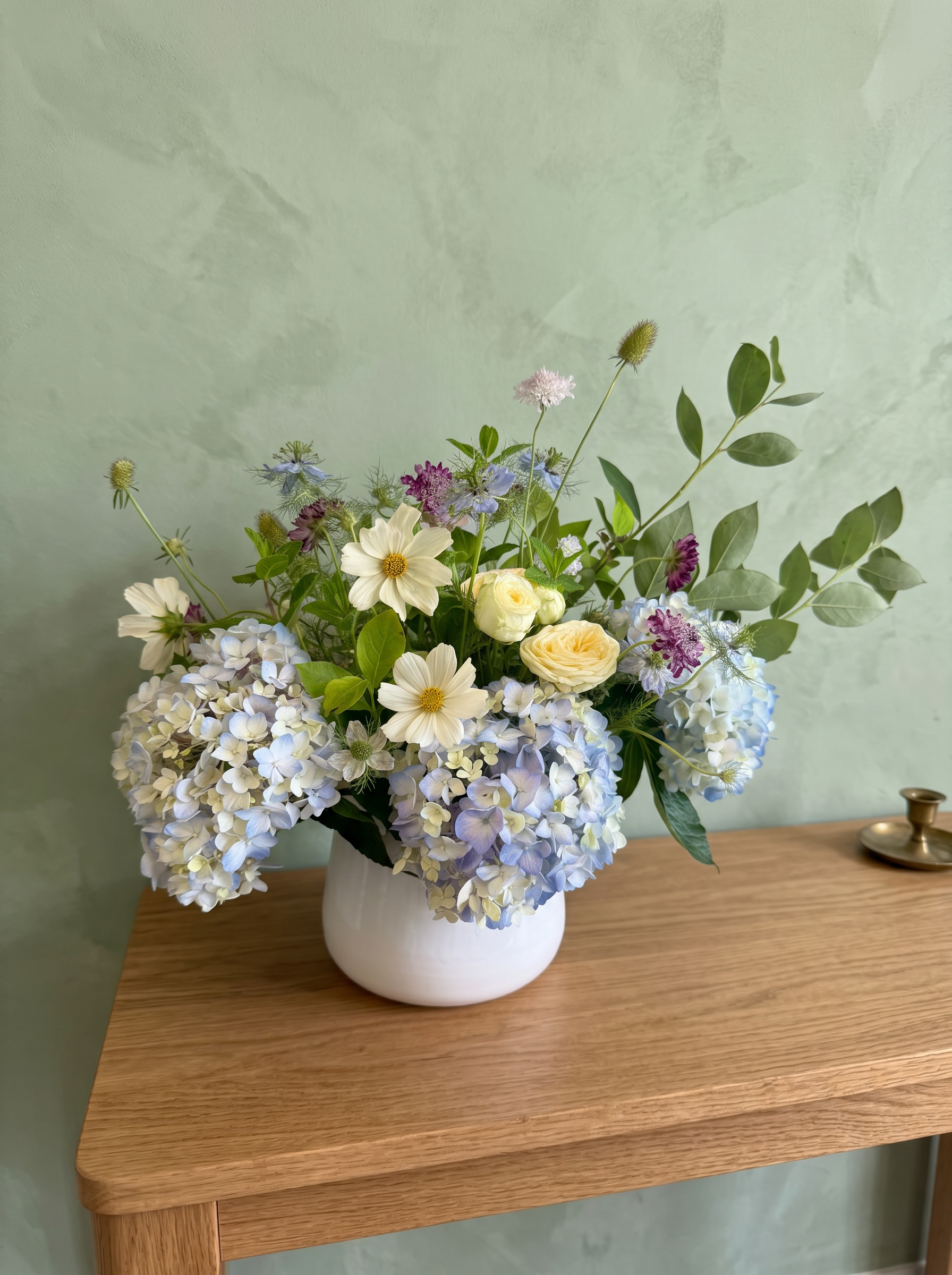 Blue hydrangea, cream cosmos and butter roses in a white ceramic vase