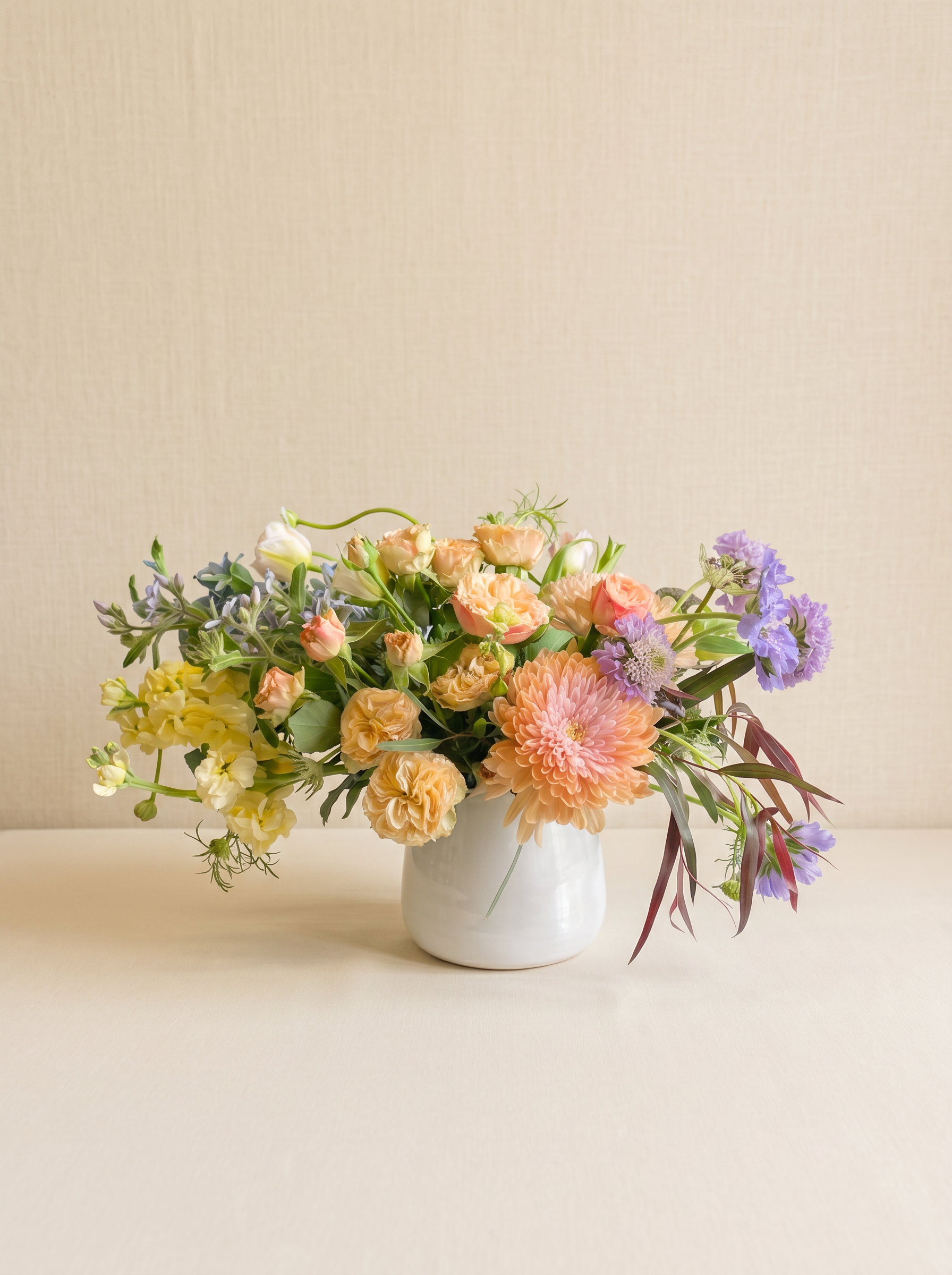 Peach garden roses, dahlia and lavender scabiosa in a white ceramic vase