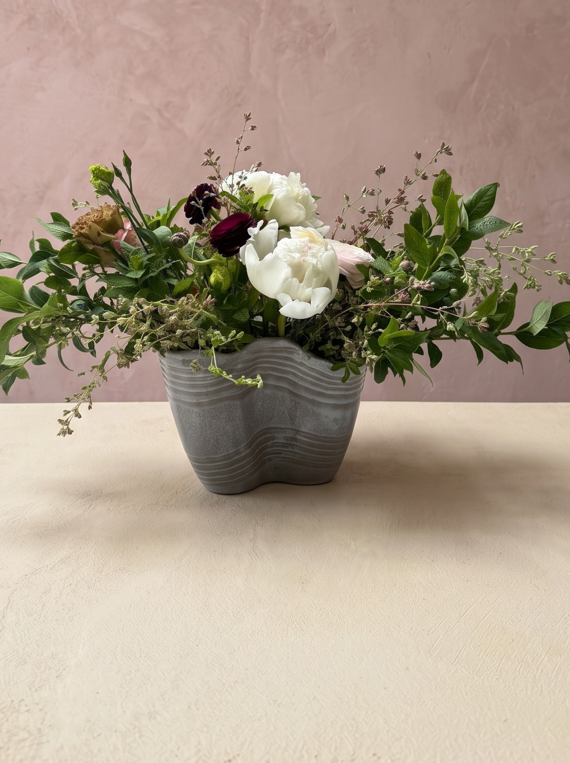 Wild greenery and white peony arrangement in a sculptural stone vessel