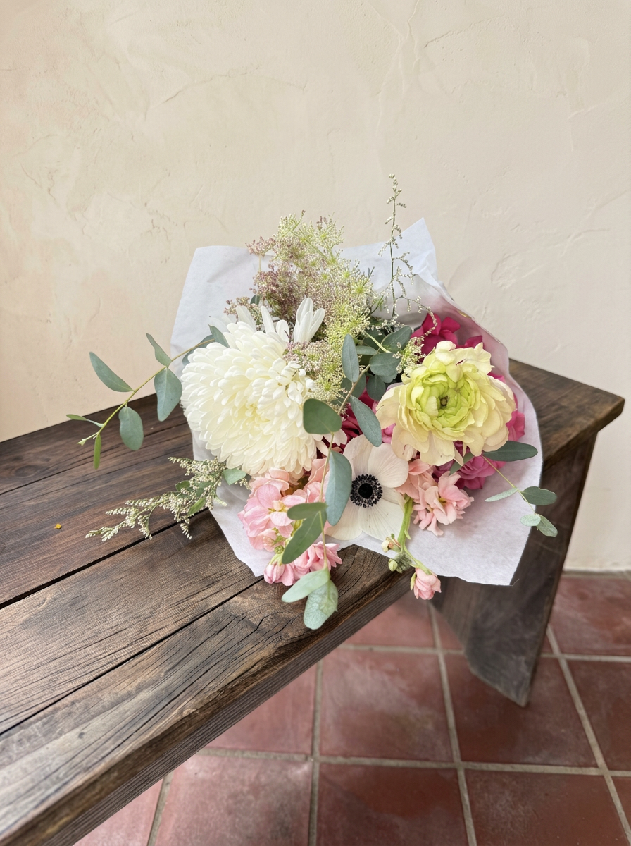 White chrysanthemum, ranunculus and anemone bouquet resting on a wood bench