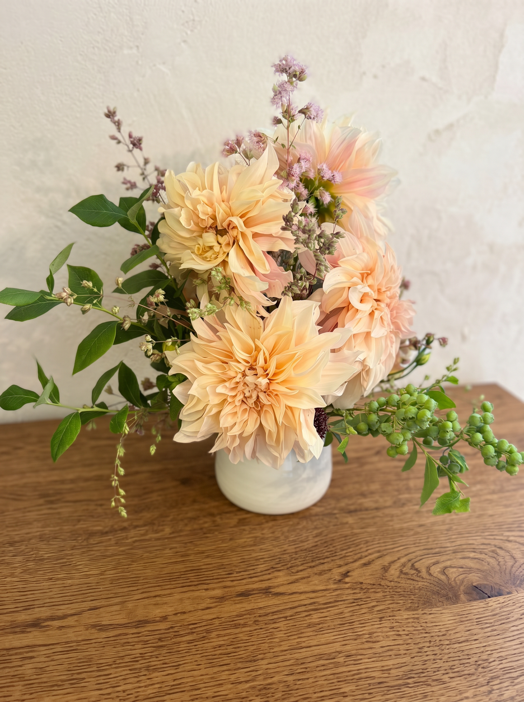 Café au lait dahlias with pink ageratum and greenery in a white ceramic vase